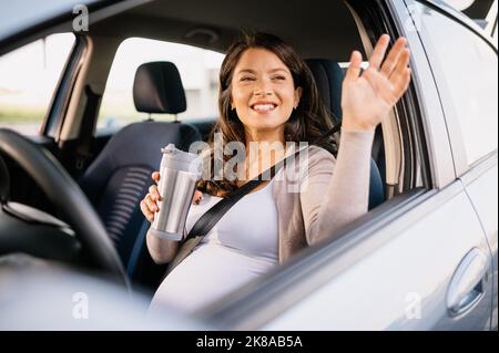 Schwanger kaukasische Frau mit glücklichen Gesicht im Auto sitzen und winken mit der Hand Stockfoto