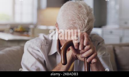 Depression kommt von zu viel Zeit im Kopf. Ein älterer Mann sitzt allein auf dem Sofa zu Hause und fühlt sich deprimiert, während er seine hält Stockfoto