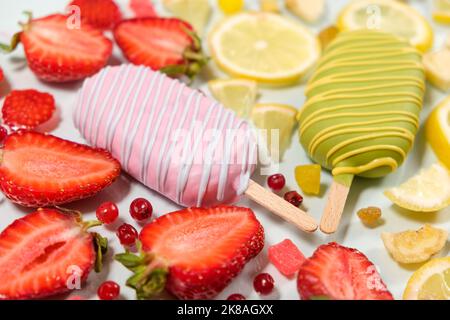 Zwei Eiscremes auf einem Stock - Erdbeere und Zitrone auf weißem Hintergrund. Sommerliche Fruchtdesserts. Stockfoto