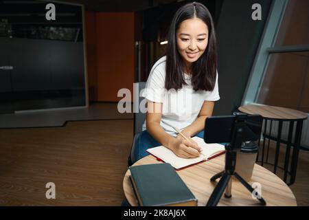 Charmante Frau, die sich Notizen beim Meisterkurs auf dem Smartphone anhört Stockfoto