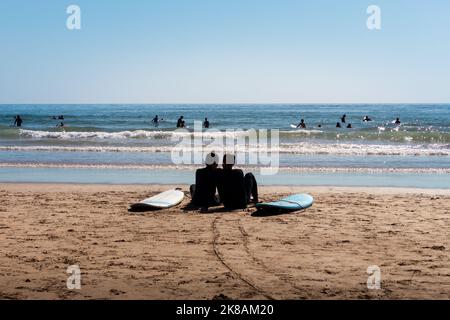 Surferpaar, das sich vom Surfen im Neoprenanzug am Strand von Arrifana, Algarve, Portugal, ausruhte Stockfoto