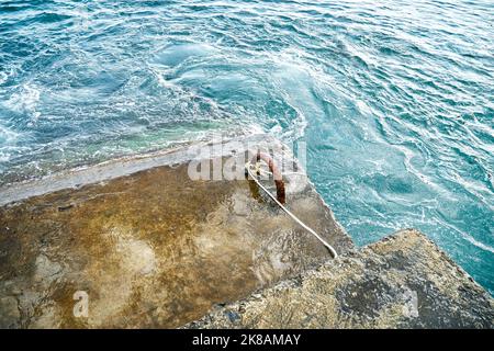 Altes Stahlbeton-Wellenbrechwasser mit Metallschlaufen und Seil im brodelnden Meer Stockfoto