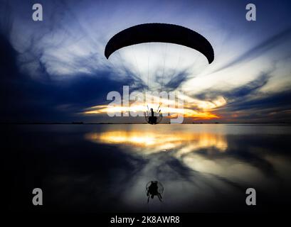 Motorbetriebener Gleitschirm, der während des Sonnenuntergangs über dem See läuft. Extremsport und Adrenalin in der Luft Stockfoto