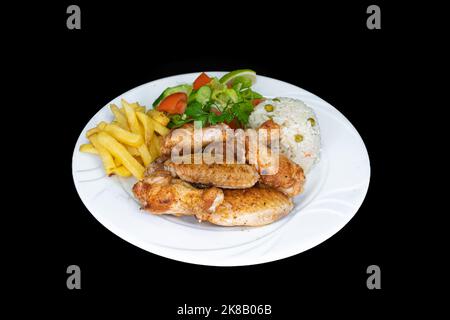 Gegrillte Hähnchenflügel mit Reis, Salat und pommes auf einem weißen Teller auf schwarzem Hintergrund Stockfoto