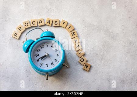 Procrastination Text mit blauem Wecker auf betontem Hintergrund. Zeitmanagement-Konzept. Stockfoto
