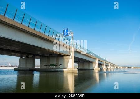 Die Zeeburgerbrücke nach Amsterdam IJburg über das gefrorene Wasser der nieuwe Diep aus dem Diemerzeedijk. Mit der gläsernen Lärmschutzwand. Stockfoto