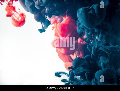 Rote und blaue Acryltinten in Wasser, die einen abstrakten Hintergrund mit weißem Kopierbereich bilden. Stockfoto