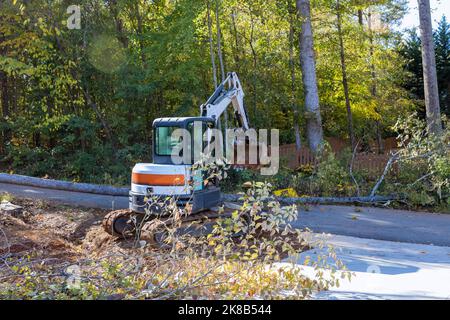 Gefallener Baum nach Sturm beschädigter Zaun nach Hurrikan eine entwurzelte Bäume fiel auf die Straße, wobei der Traktor aufräumte, um umgestürzte Bäume aufzurichten Stockfoto