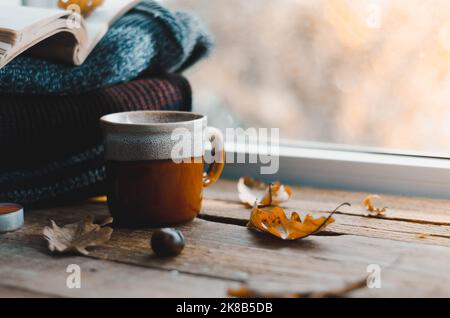 Große Tasse Cappuccino auf vintage braunem Hintergrund. Herbst, Herbstblätter, heiße, dampfende Tasse Kaffee und ein warmer Schal auf Holztischhintergrund. Meere Stockfoto