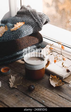 Große Tasse Cappuccino auf vintage braunem Hintergrund. Herbst, Herbstblätter, heiße, dampfende Tasse Kaffee und ein warmer Schal auf Holztischhintergrund. Meere Stockfoto