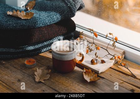 Große Tasse Cappuccino auf vintage braunem Hintergrund. Herbst, Herbstblätter, heiße, dampfende Tasse Kaffee und ein warmer Schal auf Holztischhintergrund. Meere Stockfoto