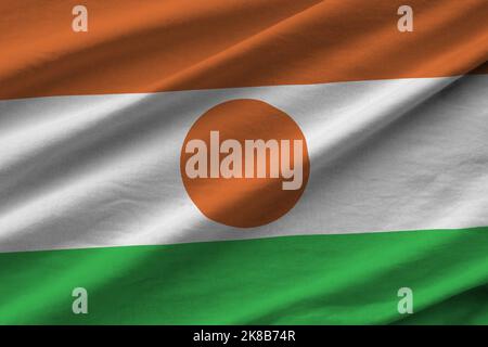 Niger-Flagge mit großen Falten, die aus nächster Nähe unter dem Studiolicht im Innenbereich winken. Die offiziellen Symbole und Farben in Stoff Banner Stockfoto