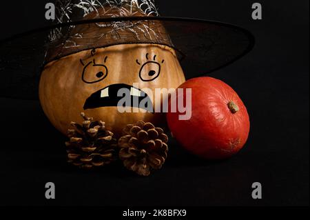 Ein Kürbis in Zauberer Hut mit einem gruseligen Gesicht, Pinienzapfen, auf schwarzem Hintergrund. Jack-O-Lantern. Halloween Trick and Treat Stockfoto