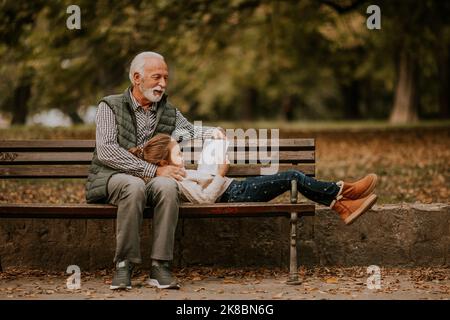 Der gutaussehende Großvater verbringt am Herbsttag Zeit mit seiner Enkelin auf der Bank im Park Stockfoto