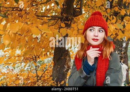 Verträumte Frau mit roten Haaren und schwarzen Augen genießen die Natur im Herbstwald. Gelbe Blätter. Stockfoto
