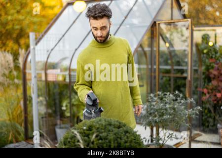 Guy schneidet einen runden Busch mit einer Schere Stockfoto