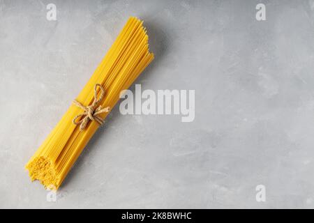Rohe Spaghetti mit Garn auf grauem Hintergrund gebunden. Gelbe ungekochte Pasta-Spaghetti auf Beton. Draufsicht. Speicherplatz kopieren Stockfoto