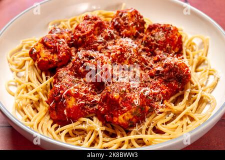Putenfleischbällchen mit Knoblauch- und Basilikumtomatensauce und Vollkornteigwaren, die mit Parmesan auf dem Teller bestreut wurden Stockfoto