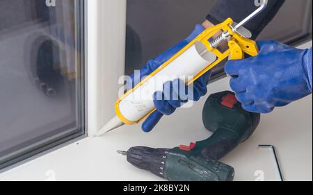 Bauarbeiter versiegelt Fenster mit Versiegelung in Innenräumen Stockfoto