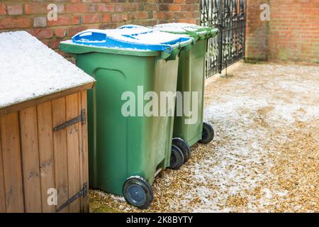 Grüne und blaue Mülltonnen in einem im Winter schneebedeckten Garten, Großbritannien Stockfoto