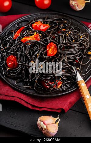 Schwarze Spaghetti mit Gemüse auf schwarzem Teller. Gekochte schwarze Pasta-Spaghetti auf schwarzen Brettern und Zutaten. Nahaufnahme Stockfoto