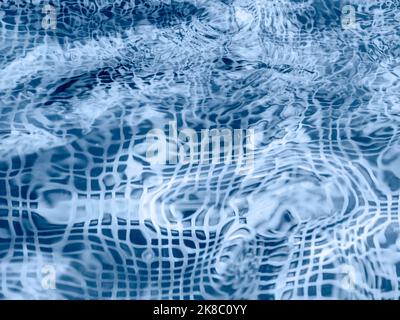 Wasseroberfläche im Schwimmbad oder Springbrunnen mit blauem Mosaikboden. Abstrakter Hintergrund mit Wellenmuster aus klarem, transparentem Wasser. Stockfoto