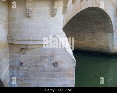 Fluss, der unter einer Steinbrücke mit kleinen Wasserspeier-Gesichtern in Paris, Frankreich, fließt. Stockfoto