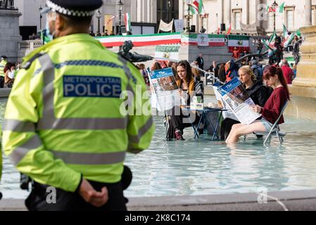 London, Großbritannien. 22. Oktober 2022. Tierrechtsaktivisten Animal Rebellion färbt Trafalgar Square-Brunnen grün, während sie an einem Tisch sitzen und eine Zeitung lesen. Der Protest folgt auf Kommentare der ehemaligen Innenministerin Suella Braverman, die die Aktivisten als "Hüterlesung, Tofu-Essen, Wokerati" bezeichnete. Die Aktivisten fordern eine Transaktion zum pflanzenbasierten Ernährungssystem und für die Regierung, das Land zurückzugeben. Quelle: Andrea Domeniconi/Alamy Live News Stockfoto