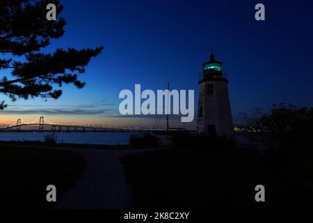 Goat Island Lighthouse mit der Newport Bridge im Hintergrund in der Abenddämmerung in Rhode Island Stockfoto