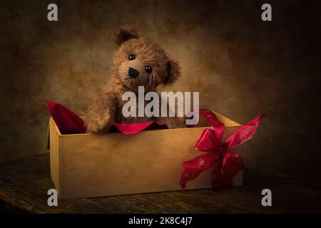 Niedlicher kleiner Teddybär, der in einer Holzkiste mit Geschenkband versteckt ist. Stockfoto