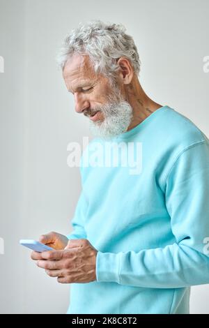 Älterer bärtiger Hipster-Mann, der ein Mobiltelefon an einer weißen Wand benutzte. Stockfoto