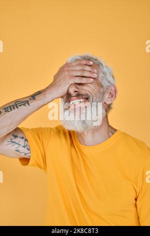 Lächelnder, lustiger, älterer bärtiger tätowierte Mann, der isoliert auf Gelb lachte. Stockfoto