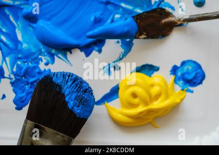 Overhead-Aufnahme von Bürsten für die Malerei, Pfütze aus blauer und gelber Farbe, Acrylfarbe auf hellem Brett. Kunstkonzept. Kunsthochschule Stockfoto