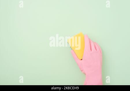 Hand in rosa Gummihandschuh mit gelbem Schwamm auf hellgrünem Hintergrund. Draufsicht, flach liegend, Kopierbereich Stockfoto