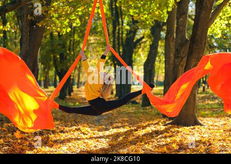 Frau, die im Herbst auf einem Baumhintergrund Luftseide übt Stockfoto