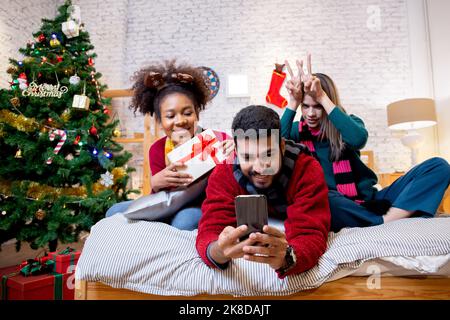 Gruppe junge Freunde nehmen Selfie mit aufgeregt und genießen Sie mit Smartphone zusammen zu Hause, Mann und Frau machen ein Foto in der Feier Heiligabend mit Stockfoto