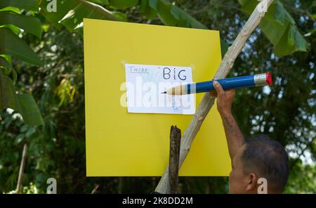 Ein Künstler, der in einem tropischen Garten mit einem sehr großen Bleistift zeichnet. Stockfoto