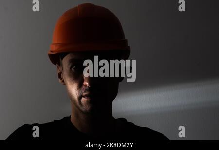 Schmutziges Gesicht des Kohlebergarbeiters auf schwarzem Hintergrund. Kopf eines müden Bergarbeiters in einem Hut. Stockfoto