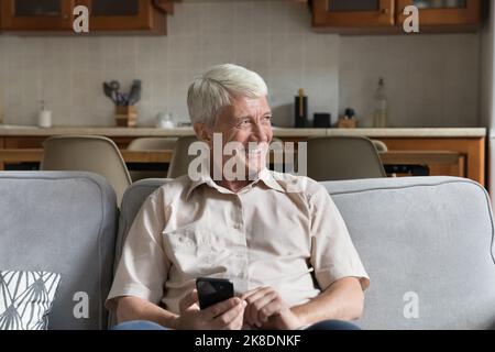 Reifer Single-Mann sitzt auf dem Sofa mit modernem Smartphone Stockfoto