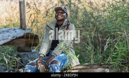 Die Afrikanerin sitzt an einem sonnigen Herbsttag draußen auf einer Holzeiche in der Natur Stockfoto