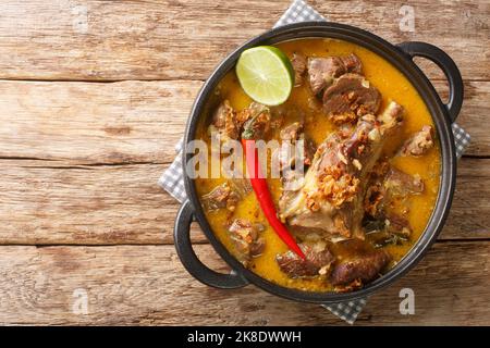 Indonesisches Essen Gulai Kambing Ziegenkurvig würziger Eintopf aus der Nähe auf der Pfanne auf dem Holztisch. Horizontale Draufsicht von oben Stockfoto