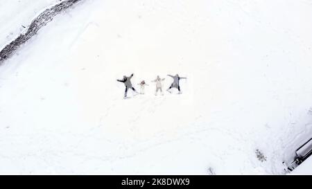 Winterspaß für die ganze Familie. Glückliche Familie von 4 machen Engel auf dem Schnee. aero, Draufsicht. Die Familie genießt Schnee und Schneefall und hat Spaß am verschneiten Wintertag im Freien. Hochwertige Fotos Stockfoto