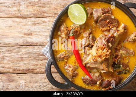 Gulai Kambing traditioneller javanischer Hammelfleisch-Eintopf aus der Nähe auf der Pfanne auf dem Holztisch. Horizontale Draufsicht von oben Stockfoto