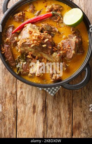 Gulai Kambing ist ein traditionelles indonesisches Essen, das ein reiches, würziges und sukkkkulentes, in der Pfanne auf dem Holztisch anhaltendes, herzliches und würziges Gericht enthält. Vertikal Stockfoto