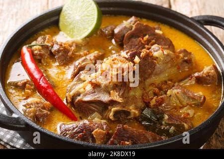 Gulai Kambing traditioneller javanischer Hammelfleisch-Eintopf aus der Nähe auf der Pfanne auf dem Holztisch. Horizontal Stockfoto