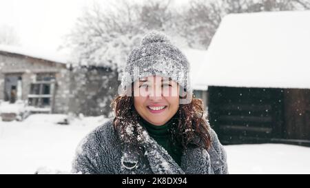 Schneereichen Winterspaß. Schneeverwehung. Eine glückliche Frau, die in warme Winterkleidung gekleidet ist, bläst Schnee aus den Händen der Kamera, im Freien, in verschneiten Parks oder Wäldern. Hochwertige Fotos Stockfoto