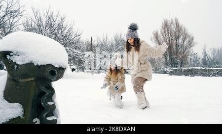 Winter Familienaktivitäten im Freien. Seitenansicht. Glückliche kleine Mädchen, Kinder laufen langsam durch dicken Schnee im Stadtpark, während Schneefall. Familie hat Spaß, verbringen Zeit zusammen am verschneiten Wintertag. Zeitlupe. Hochwertige Fotos Stockfoto