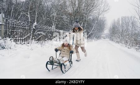 Familienrodeln im Winter. Outdoor Winteraktivitäten. Fröhliche, lachende, verspielte Kinder genießen das Rodeln auf verschneiten Straßen, im Wald, bei Schneefall. Kinder haben Spaß an verschneiten Wintertagen. Zeitlupe. Hochwertige Fotos Stockfoto