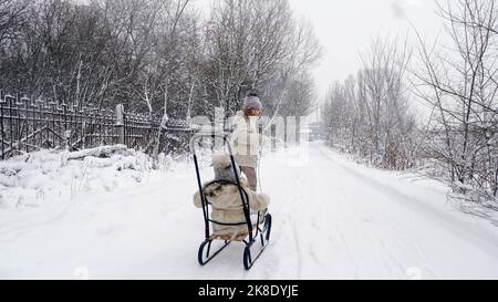 Familienrodeln im Winter. Outdoor Winteraktivitäten. Fröhliche, lachende, verspielte Kinder genießen das Rodeln auf verschneiten Straßen, im Wald, bei Schneefall. Kinder haben Spaß an verschneiten Wintertagen. Zeitlupe. Hochwertige Fotos Stockfoto