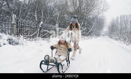 Familienrodeln im Winter. Outdoor Winteraktivitäten. Fröhliche, lachende, verspielte Kinder genießen das Rodeln auf verschneiten Straßen, im Wald, bei Schneefall. Kinder haben Spaß an verschneiten Wintertagen. Zeitlupe. Hochwertige Fotos Stockfoto